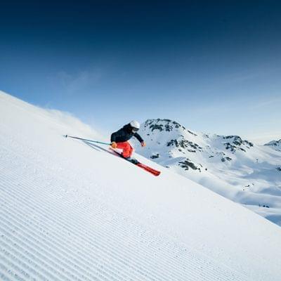 Skier carving down freshly groomed slope in sunny alpine mountain landscape